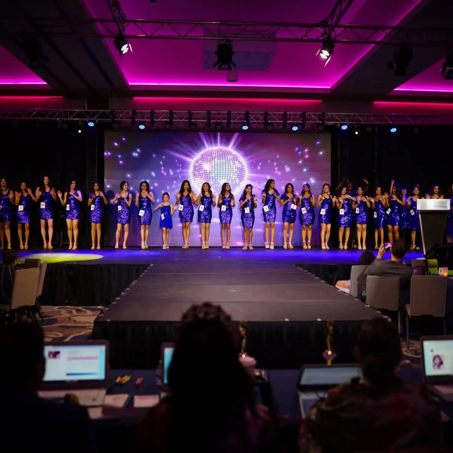 Contestants in matching sequinned dresses lined up on stage in front of the judges' table