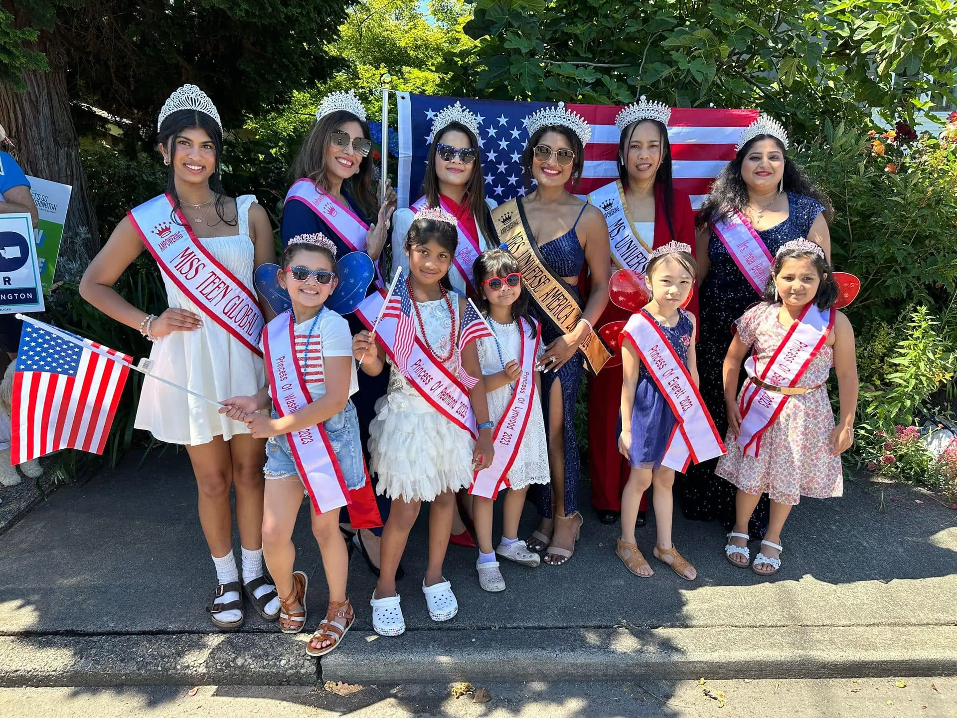 Titleholders and young girls in sashes waving American flags at a community parade