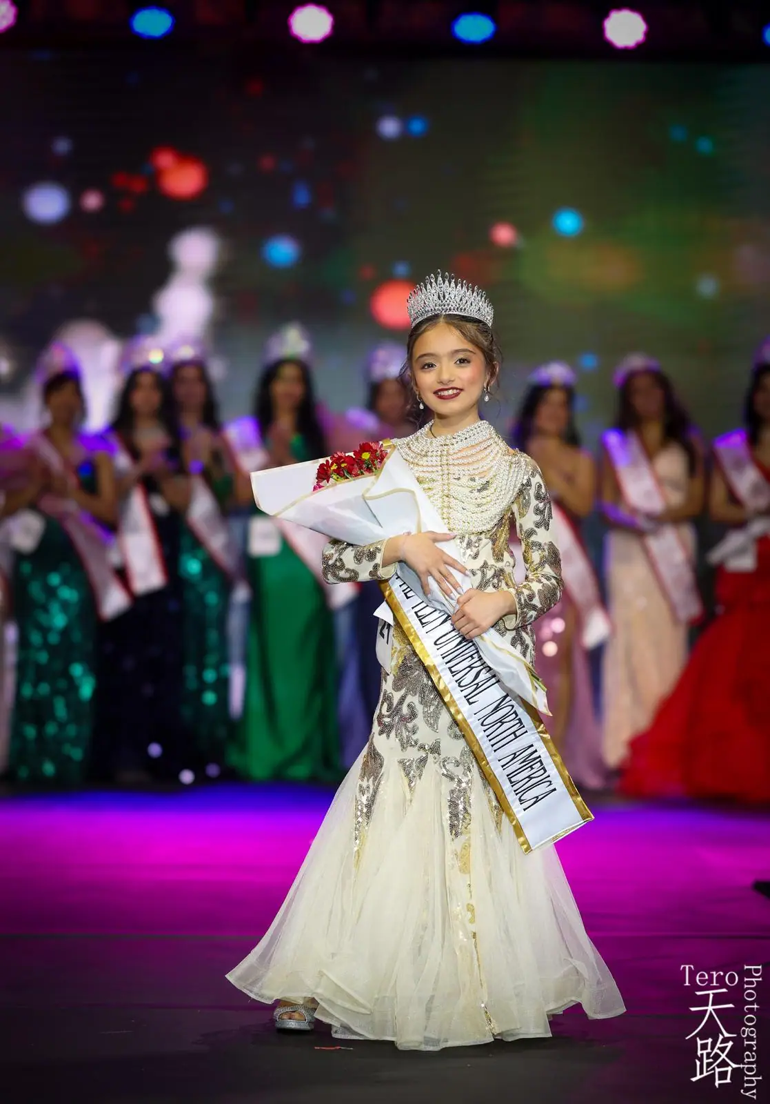 A young Universal North America titleholder crowned on stage, holding flowers. Photo: Tero Photography