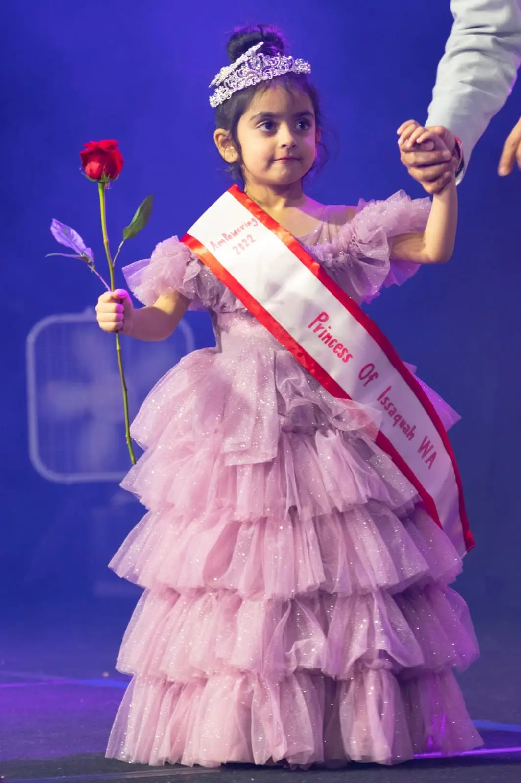 A young Princess of Issaquah WA in a tiara and lilac gown, holding a red rose on stage